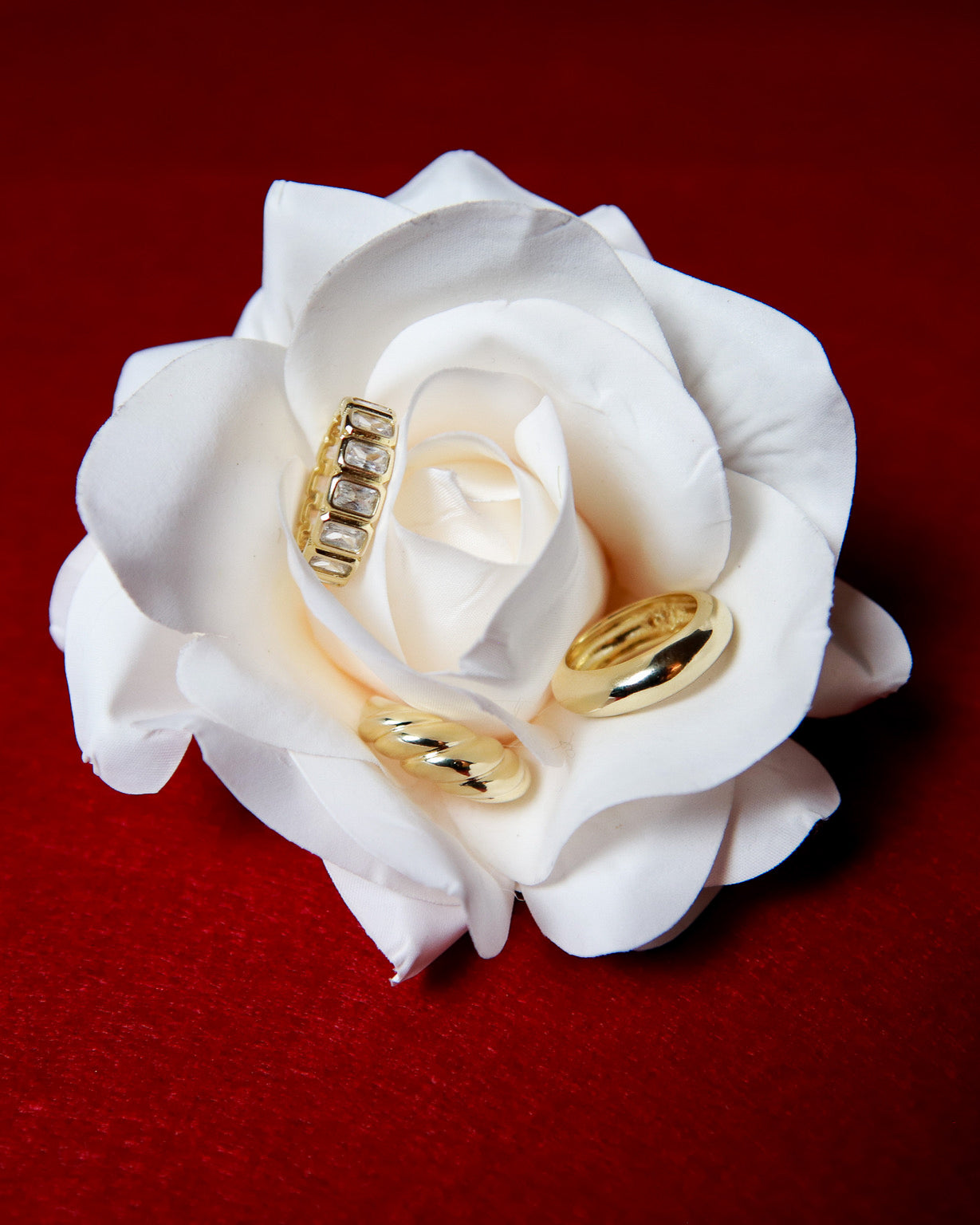 18k gold filled stacking rings and statement rings displayed on white rose against red background
