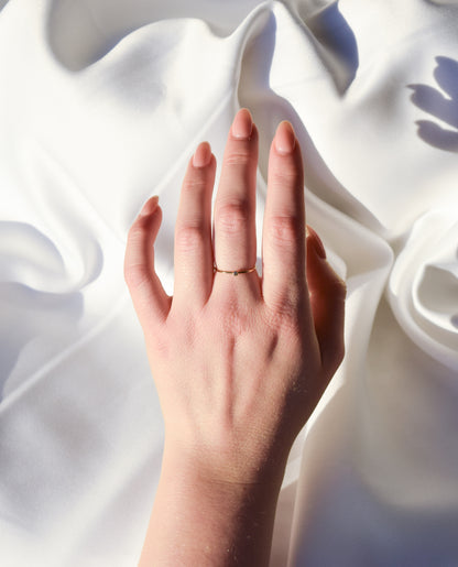 Hand wearing a delicate 14k gold filled ring with a small cubic zirconia on soft white fabric.
